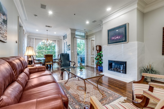 living room featuring a chandelier, wood-type flooring, crown molding, and a premium fireplace