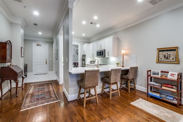 kitchen with a breakfast bar, kitchen peninsula, dark hardwood / wood-style floors, white cabinetry, and stainless steel appliances