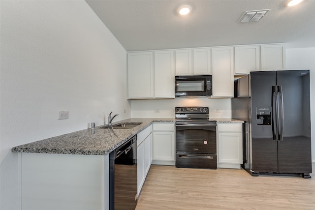 kitchen with black appliances, sink, dark stone countertops, light wood-type flooring, and white cabinetry