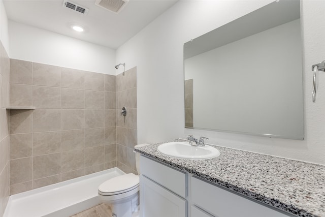 bathroom featuring a tile shower, vanity, and toilet