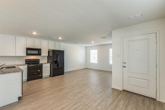 kitchen featuring light stone countertops, white cabinetry, sink, light hardwood / wood-style floors, and black appliances