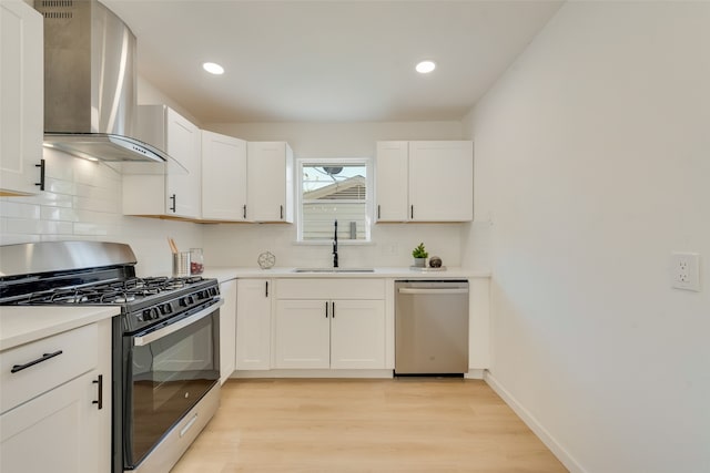 kitchen with sink, wall chimney exhaust hood, light hardwood / wood-style flooring, white cabinets, and appliances with stainless steel finishes