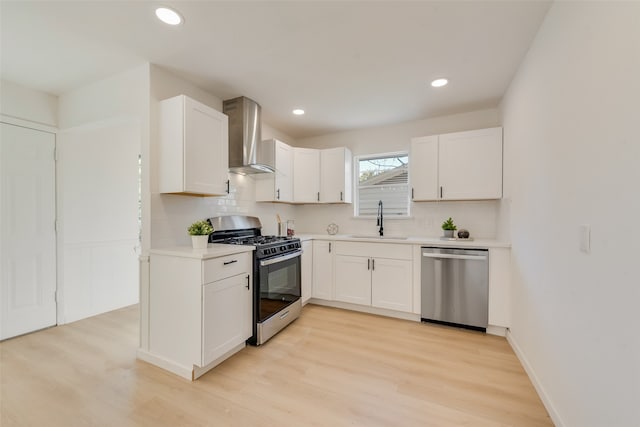 kitchen with sink, wall chimney exhaust hood, light wood-type flooring, appliances with stainless steel finishes, and white cabinetry