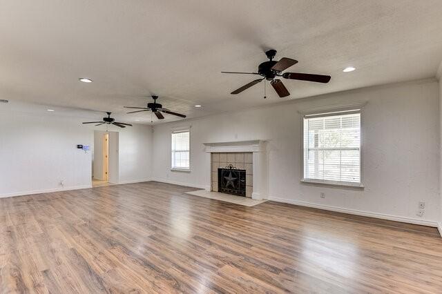 unfurnished living room featuring ceiling fan, a tile fireplace, and light hardwood / wood-style flooring