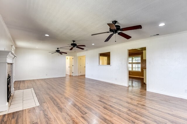 unfurnished living room featuring a fireplace, crown molding, hardwood / wood-style floors, and ceiling fan