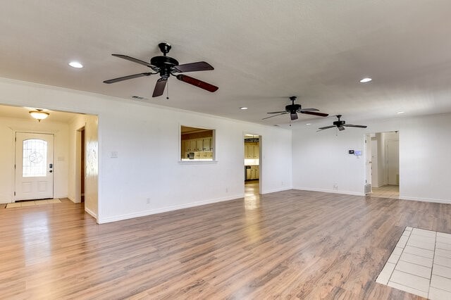 unfurnished living room featuring light hardwood / wood-style floors, ceiling fan, and crown molding