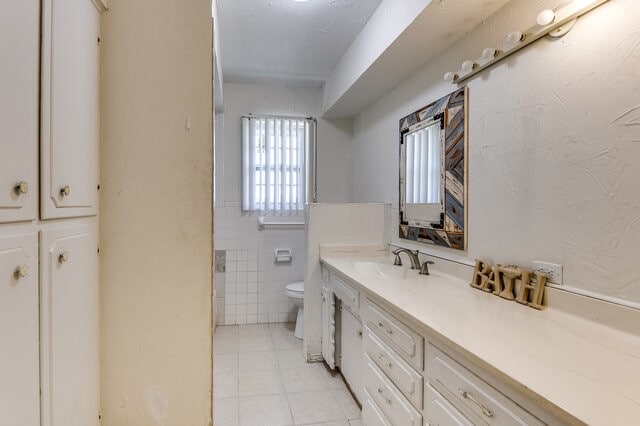 bathroom with tile patterned flooring, vanity, toilet, and tile walls