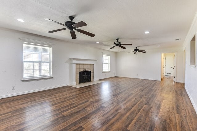 unfurnished living room featuring a tiled fireplace, ceiling fan, and dark hardwood / wood-style floors