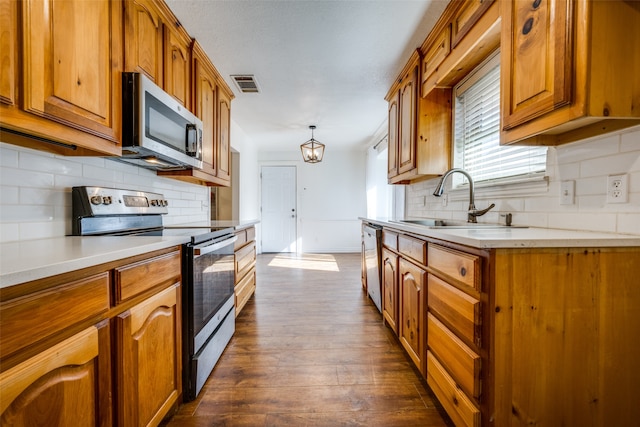 kitchen featuring sink, hanging light fixtures, appliances with stainless steel finishes, tasteful backsplash, and dark hardwood / wood-style flooring