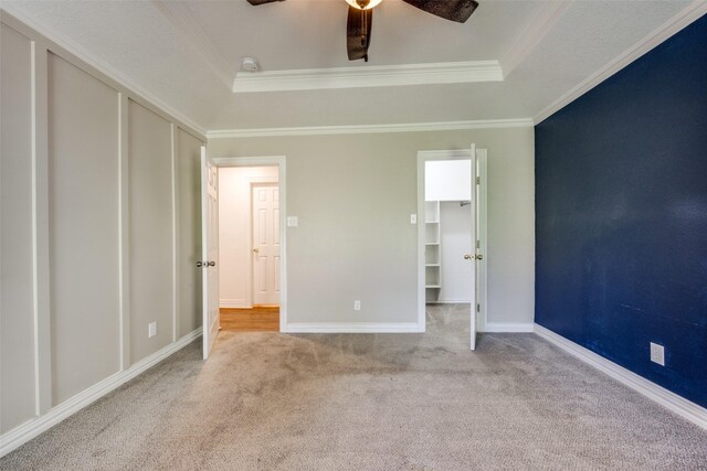 unfurnished bedroom with ceiling fan, a raised ceiling, ornamental molding, and light carpet