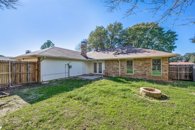 rear view of house with french doors, a fire pit, and a lawn