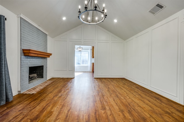 unfurnished living room with wood-type flooring, lofted ceiling, a fireplace, and a chandelier