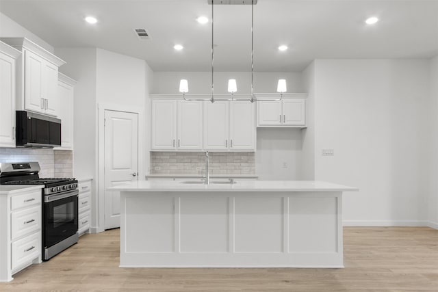 kitchen with black microwave, light countertops, white cabinets, stainless steel gas range oven, and visible vents
