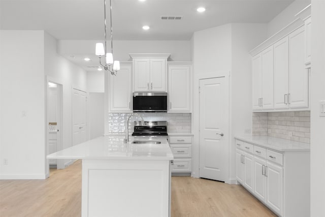 kitchen with stove, light countertops, a sink, stainless steel microwave, and white cabinetry