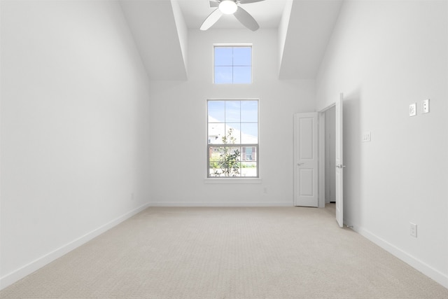 unfurnished bedroom featuring baseboards, a ceiling fan, a high ceiling, and light colored carpet