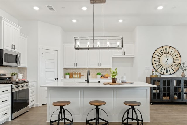 kitchen featuring an island with sink, light wood-type flooring, decorative light fixtures, and appliances with stainless steel finishes