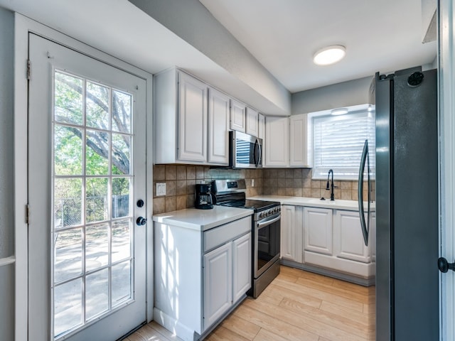 kitchen with sink, stainless steel appliances, decorative backsplash, white cabinets, and light wood-type flooring