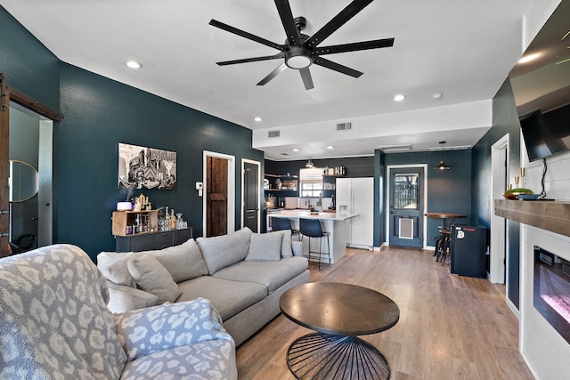 living room featuring a barn door, ceiling fan, and light hardwood / wood-style floors