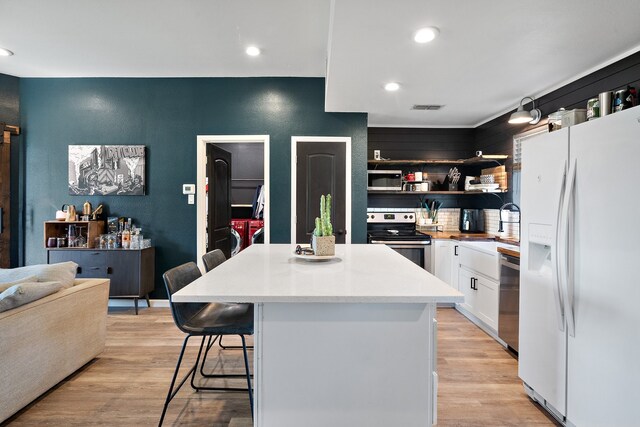 kitchen with appliances with stainless steel finishes, light wood-type flooring, a center island, white cabinetry, and a breakfast bar area