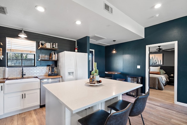 kitchen featuring white cabinets, light hardwood / wood-style flooring, stainless steel dishwasher, decorative light fixtures, and a kitchen island