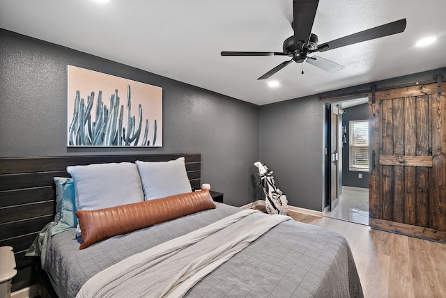 bedroom featuring a barn door, ceiling fan, and light hardwood / wood-style floors