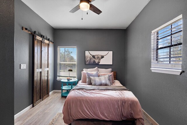 bedroom featuring ceiling fan, a barn door, light hardwood / wood-style floors, and multiple windows