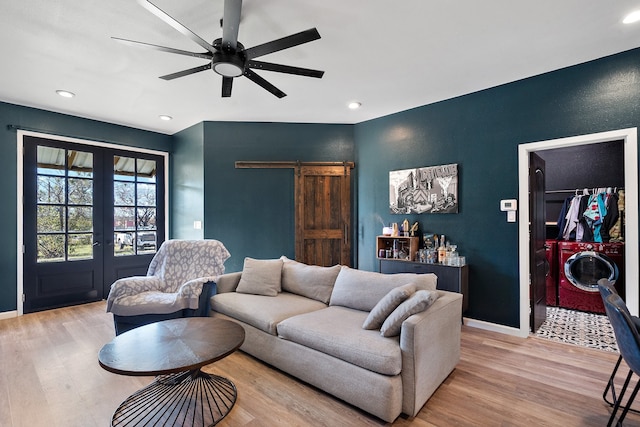 living room with french doors, ceiling fan, washer and dryer, a barn door, and light hardwood / wood-style flooring