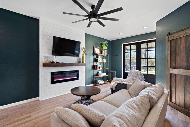 living room featuring a barn door, ceiling fan, a fireplace, and light wood-type flooring