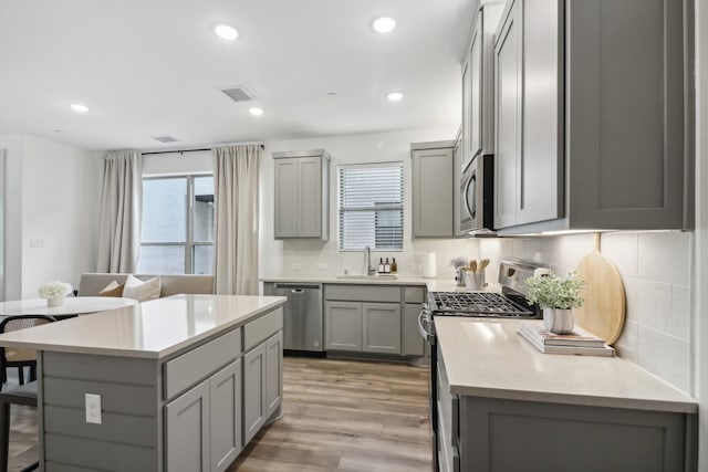 kitchen with sink, gray cabinets, light wood-type flooring, a kitchen island, and stainless steel appliances