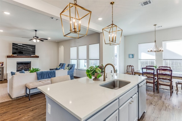 kitchen with hanging light fixtures, sink, a fireplace, and an island with sink