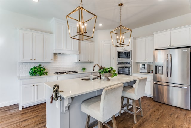 kitchen featuring stainless steel appliances, sink, a center island with sink, white cabinetry, and hanging light fixtures