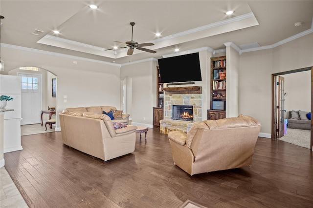 living room featuring a raised ceiling, a stone fireplace, crown molding, and dark hardwood / wood-style flooring