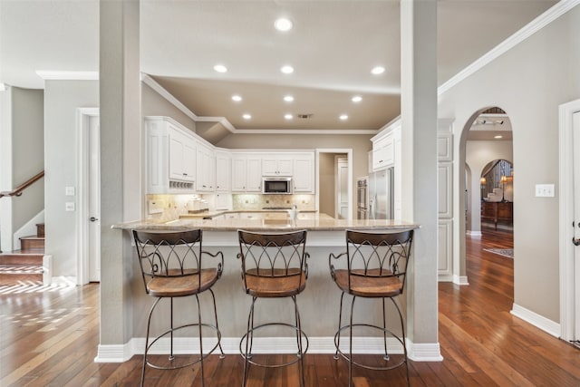 kitchen with white cabinets, dark hardwood / wood-style floors, kitchen peninsula, and stainless steel appliances