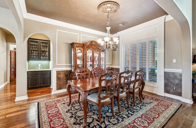 dining room with a notable chandelier, ornamental molding, a textured ceiling, and hardwood / wood-style flooring