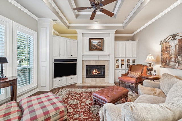 living room featuring ceiling fan, a raised ceiling, crown molding, light hardwood / wood-style floors, and a fireplace