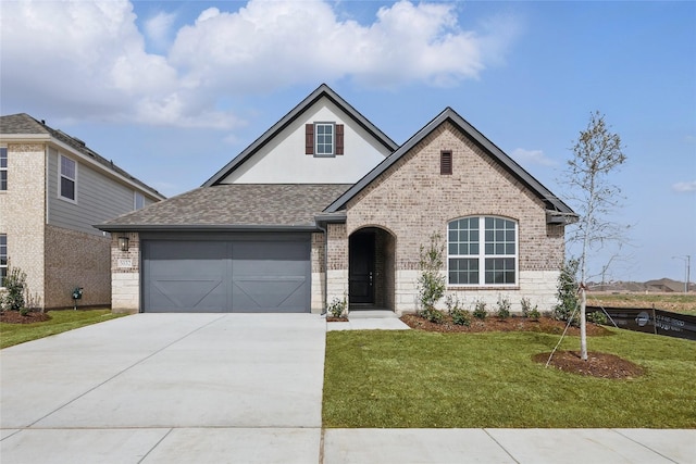 view of front of home featuring brick siding, driveway, a front lawn, and roof with shingles