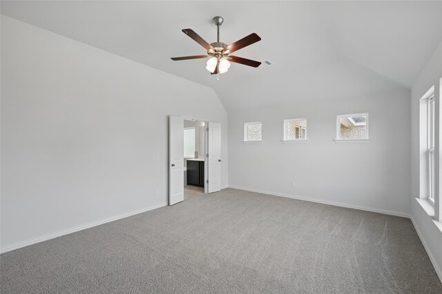 empty room with a ceiling fan, vaulted ceiling, light colored carpet, and baseboards