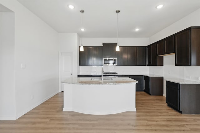 kitchen featuring a sink, stainless steel microwave, light stone counters, light wood-style floors, and dark brown cabinets