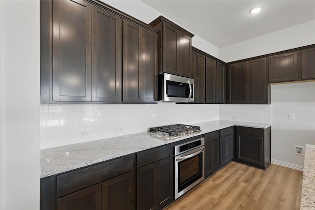 kitchen featuring tasteful backsplash, light wood finished floors, appliances with stainless steel finishes, and light stone countertops