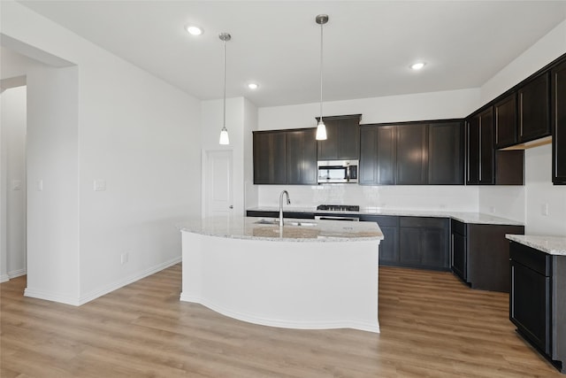 kitchen featuring stainless steel microwave, light stone countertops, light wood-type flooring, and a sink