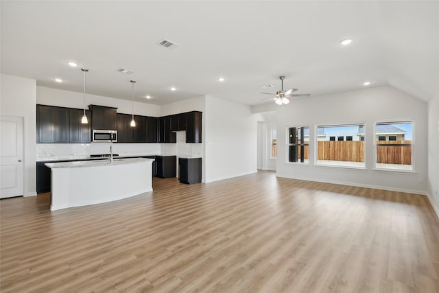 kitchen featuring light wood finished floors, stainless steel microwave, visible vents, light countertops, and a kitchen island with sink