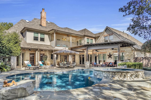 back of property with a ceiling fan, a patio area, fence, a balcony, and stone siding