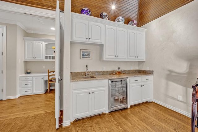 bar with sink, beverage cooler, light stone counters, and white cabinetry