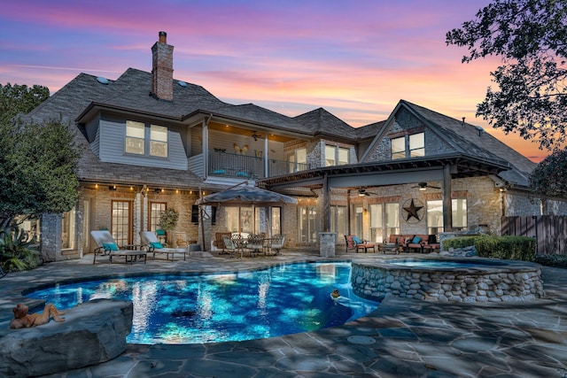 back house at dusk with ceiling fan, a patio area, a swimming pool with hot tub, and a balcony