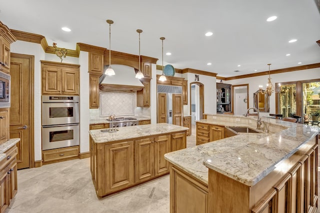 kitchen featuring a large island with sink, sink, built in appliances, hanging light fixtures, and light stone counters