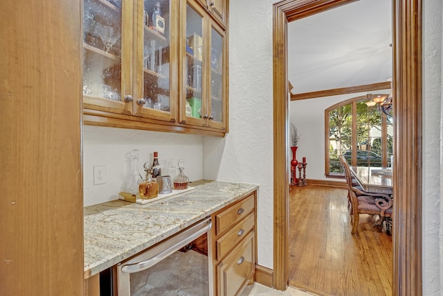 bar featuring wine cooler, light stone countertops, crown molding, and light hardwood / wood-style floors