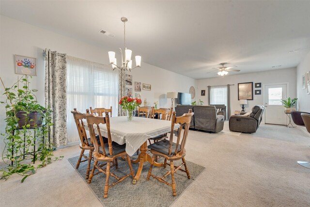 carpeted dining space with ceiling fan with notable chandelier