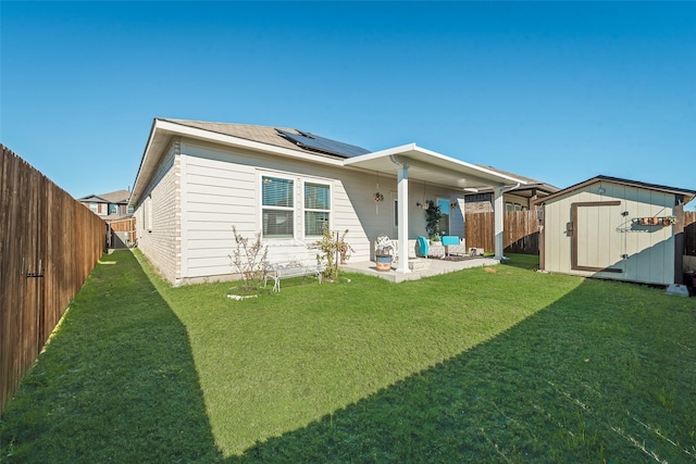 back of house with solar panels, a shed, a patio area, and a lawn