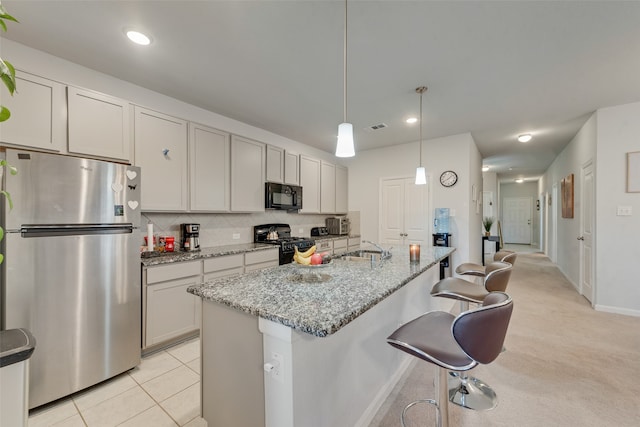 kitchen with light carpet, light stone countertops, black appliances, decorative light fixtures, and an island with sink