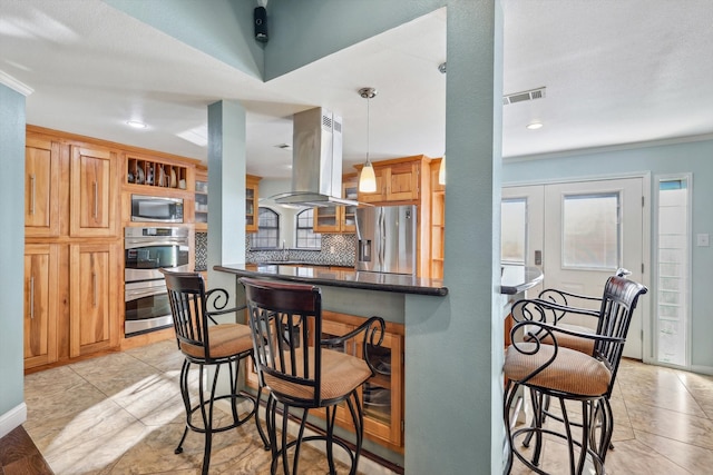 kitchen with appliances with stainless steel finishes, decorative backsplash, island exhaust hood, decorative light fixtures, and kitchen peninsula